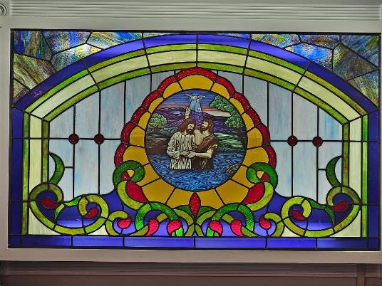 A stained glass window showing the baptism of Jesus in a Baptist church sanctuary